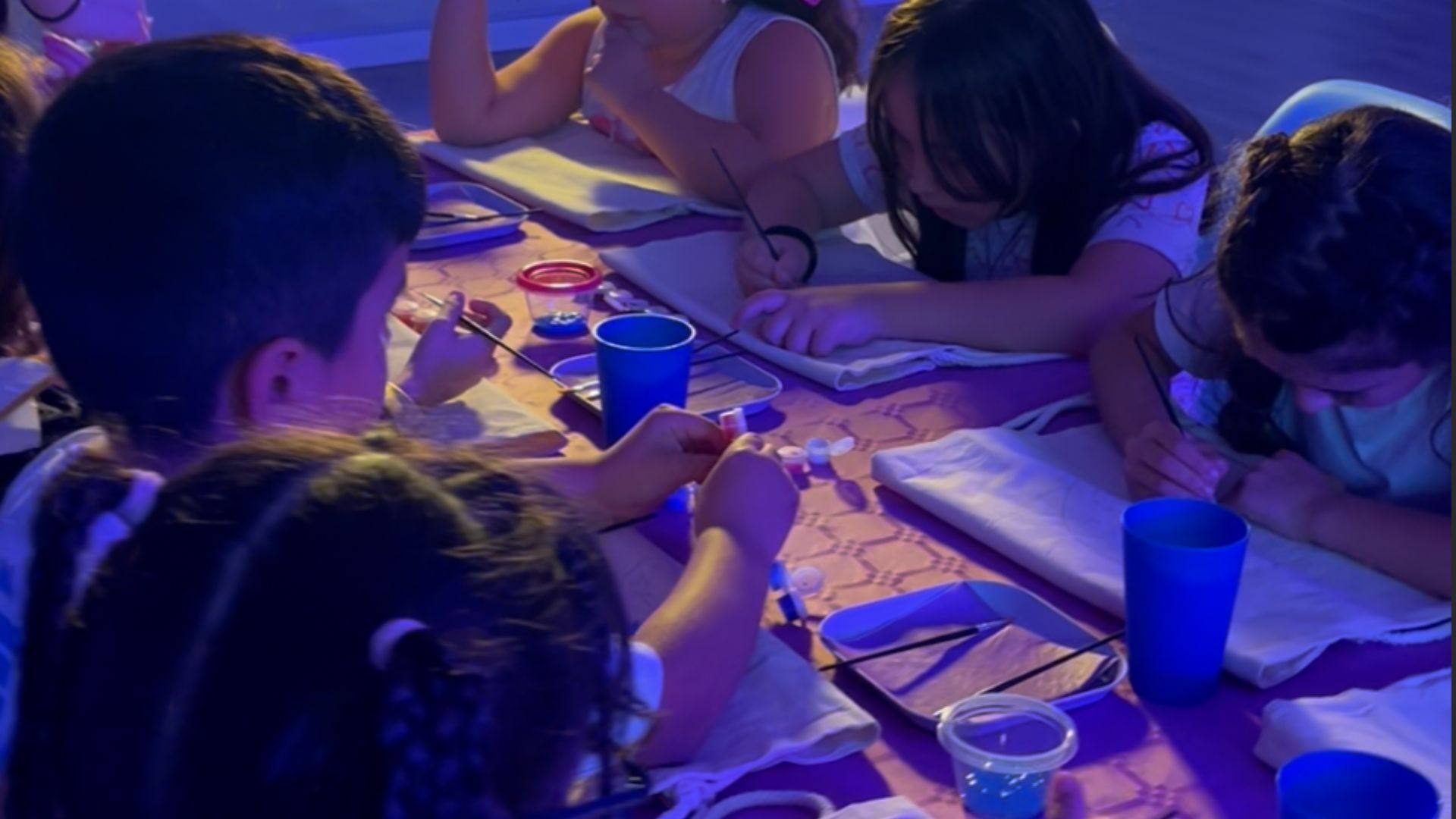 Niñas y niños haciendo manualidades en una mesa con luz azul