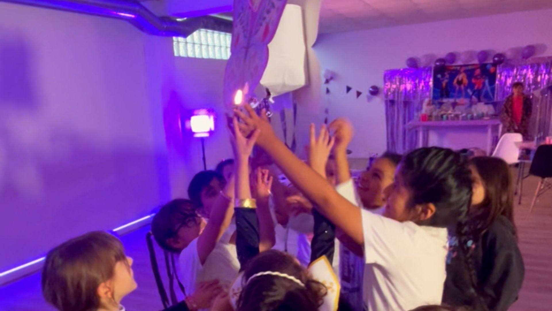 Niñas y niños con las manos en alto junto a la piñata